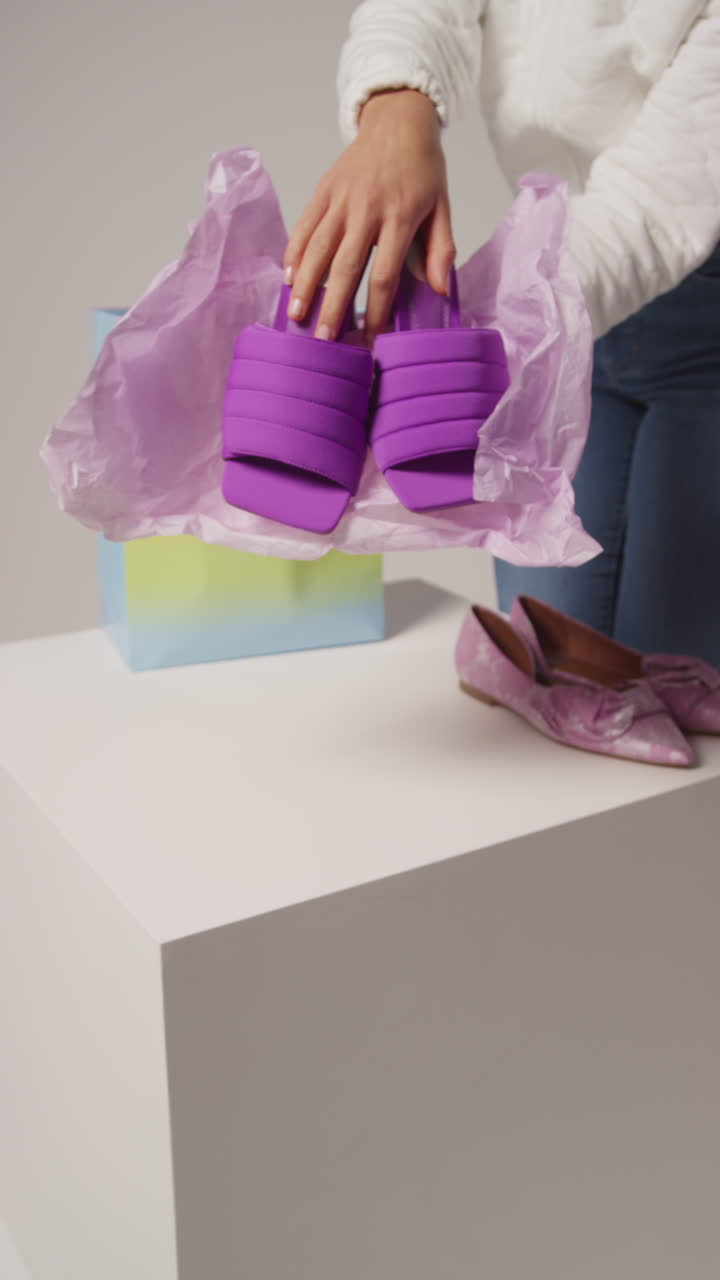 여성 소셜 미디어 인플루언서가 쇼핑 가방에서 아름다운 보라색 신발을 꺼내는 사용자 생성 콘텐츠를 생산하는 클로즈업 수직 비디오