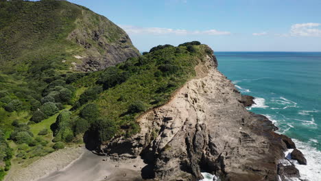 Racing-over-treetops-to-reveal-a-cove-with-turquoise-waves-breaking-on-the-rocks-in-New-Zealand