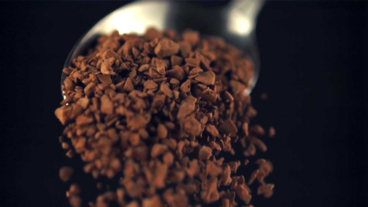 Granuli di caffè istantaneo che cadono da un cucchiaio al rallentatore