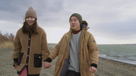 vooraanzicht van twee tiener hand in hand in winterkleren praten en wandelen aan de kust