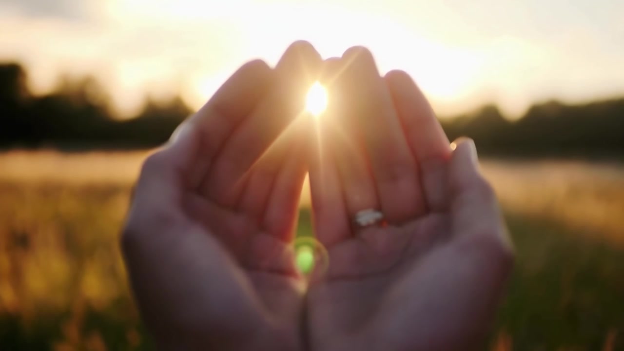 Primo piano di mani a coppa che raccolgono la luce dorata del sole al tramonto
