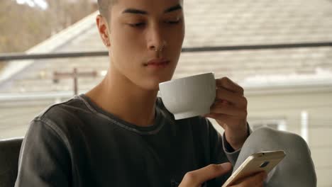 young man using mobile phone while having coffee at home 4k