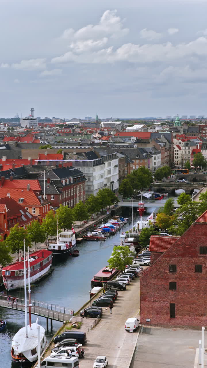 Aerial drone view of the colourful rooftops and canals of Copenhagen, with the Copenhagen City Hall tower standing prominently in the distance. Vertical