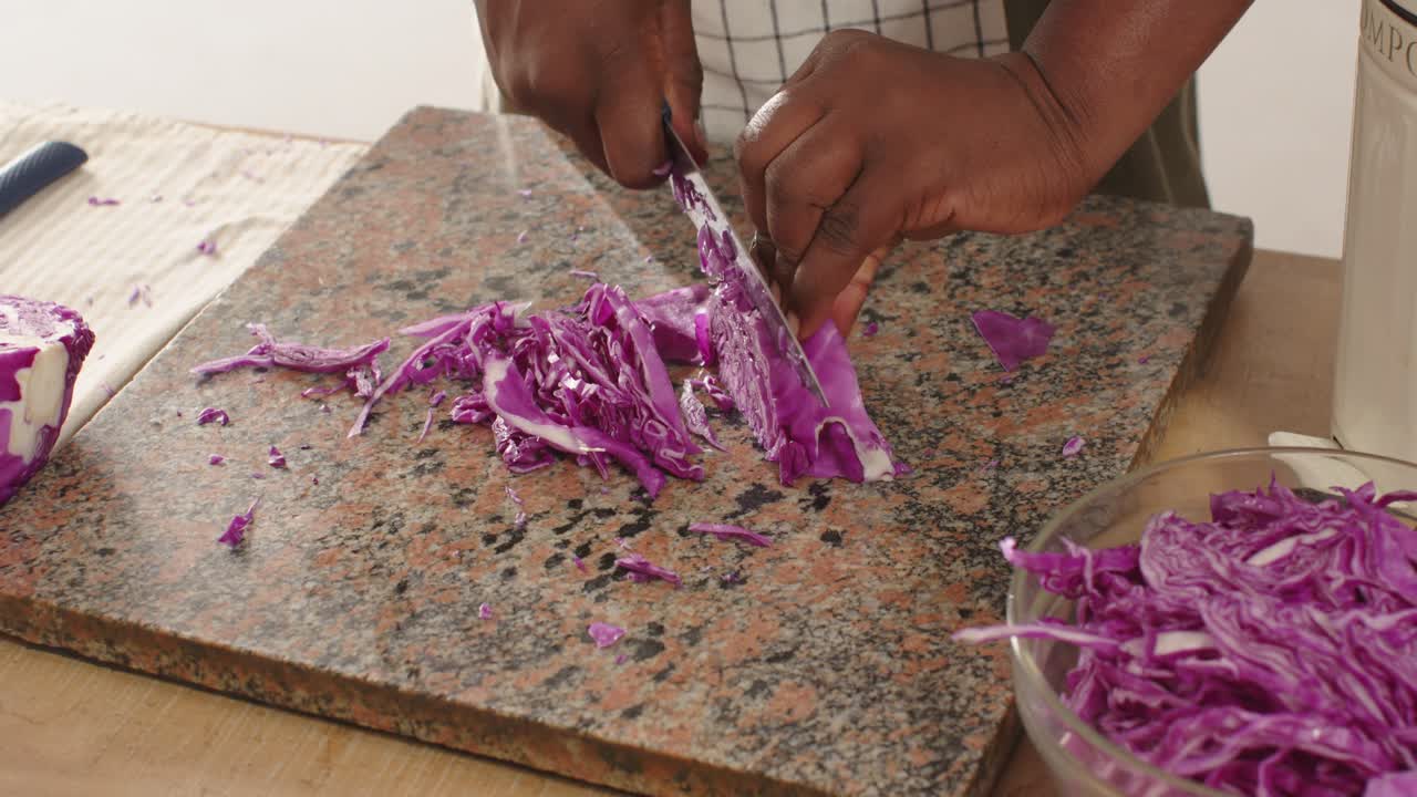 African American male placing cabbage wedge, shredding with chef's knife on granite board for slaw