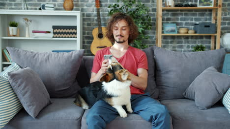 man using smartphone while sitting on couch with his dog