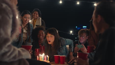 happy group of friends celebrating birthday party on rooftop at night beautiful young woman blowing candles enjoying friendship having fun sharing celebration