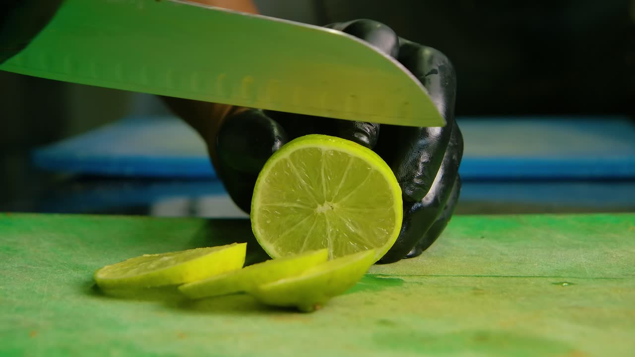 chef en guantes de látex negro limpia rebanadas de limón o lima en redondo de tamaño medio