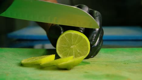 Chef in black latex gloves cleanly slices lemon or lime into medium sized round