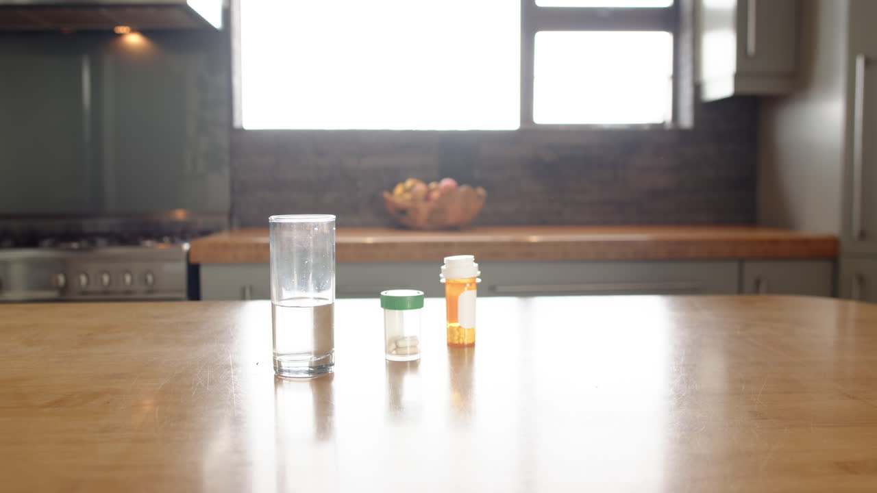 Glass of water and medication bottles on kitchen table in bright home, copy space