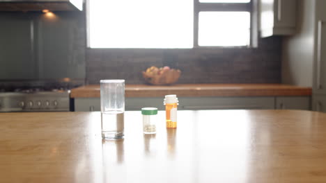 glass of water and medication bottles on kitchen table in bright home, copy space