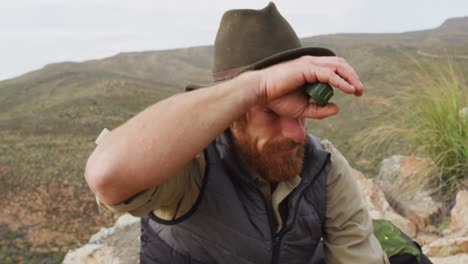 happy caucasian male survivalist sitting on mountain in wilderness, admiring the view