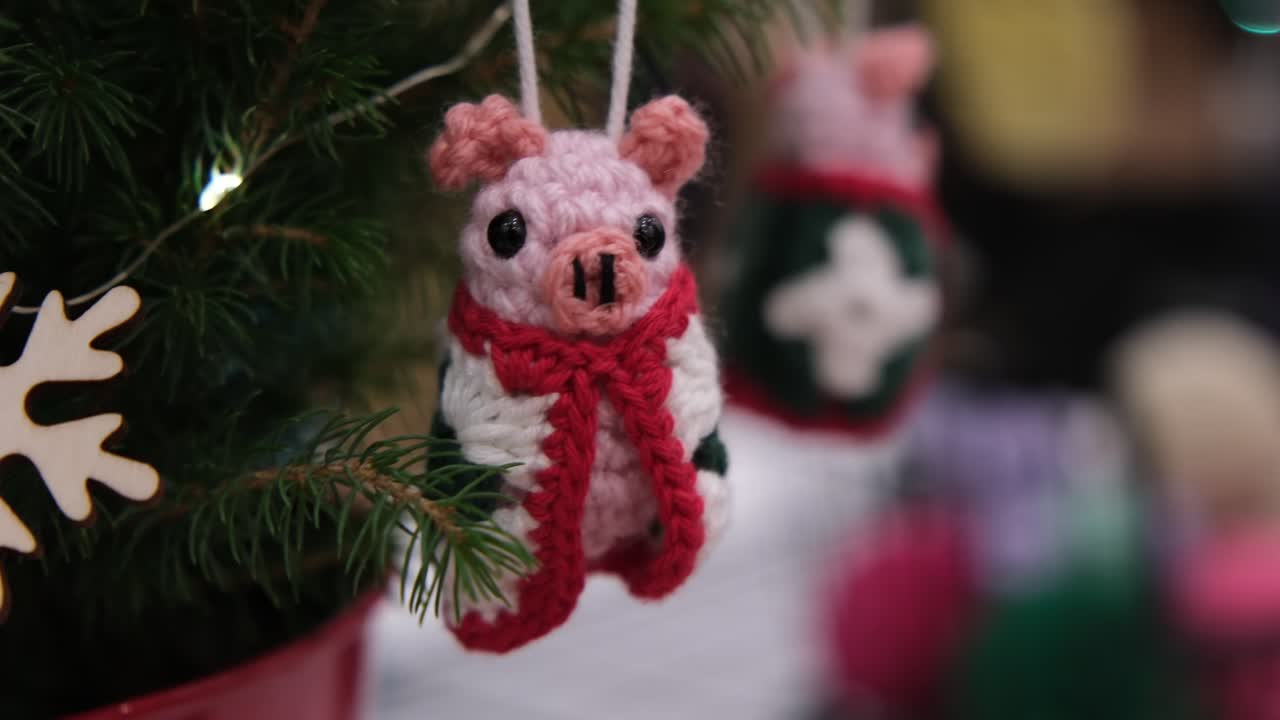Close-up camera move panning left to right while zooming out on handmade crochet pig Christmas ornaments hanging on a festive tree. Ideal for holiday, craft market, and seasonal visuals