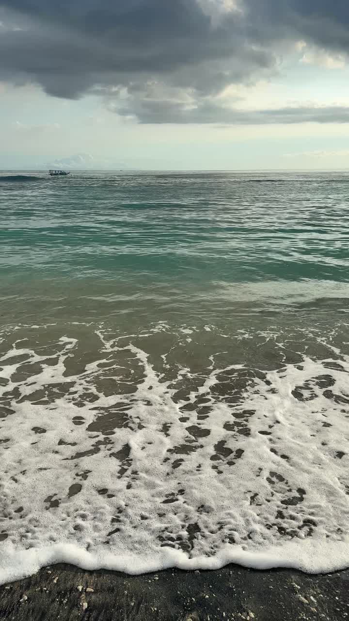 Onde dell'oceano che si infrangono dolcemente su una spiaggia di sabbia scura con una barca in lontananza