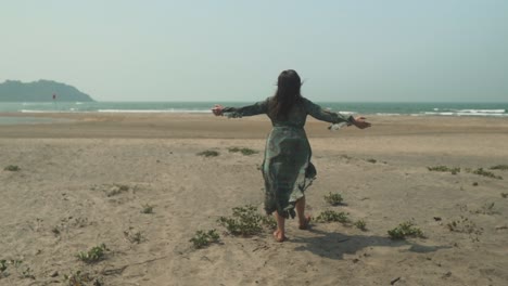 Frau-Auf-Dem-Rücken-Am-Ufer-Eines-Strandes,-Während-Der-Wind-Ihr-Kleid-Bewegt