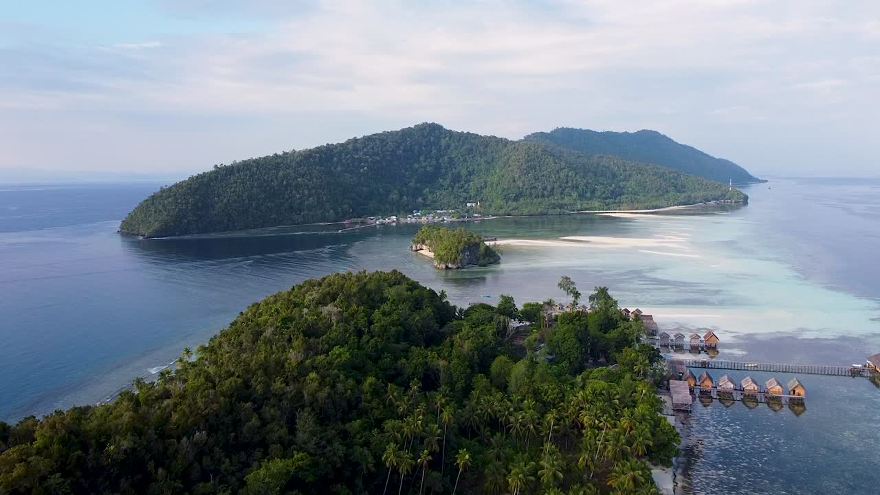 vuelo aéreo panorámico sobre islas tropicales cubiertas de selva tropical con cabañas frente al mar con vistas al océano en raja ampat, papúa occidental, indonesia