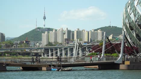 People-crossing-bridges-between-floating-islands-wearing-masks---Sebitseom-Seoul-Floating-Island-,-N-Seoul-Tower-or-Namsan-Tower-on-background