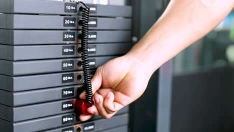 A hand adjusts the weight stack on gym equipment, setting it to 50kg. Bright lighting highlights the action