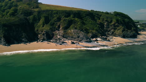 drone at sea travelling towards a sandy beach with cliffs behind