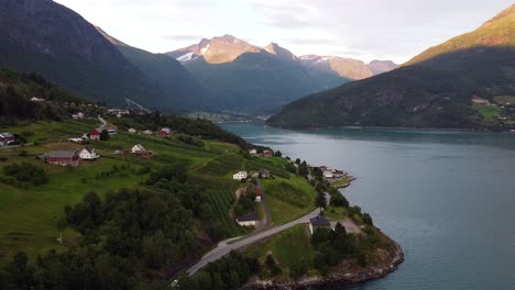 A-picturesque-road-near-Stryn,-Vestland,-Norway,-with-charming-houses,-lush-greenery,-and-majestic-mountains-in-the-background