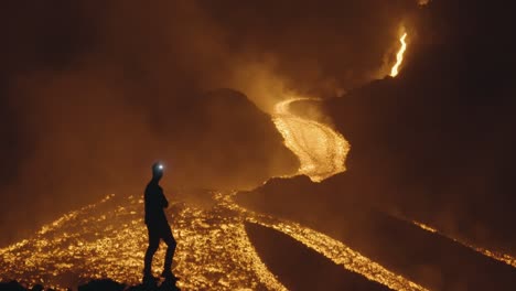 pacaya volcano, guatemala - a silhouette of a man wearing a headlamp stands at night, close to the rivers of molten lava - handheld shot