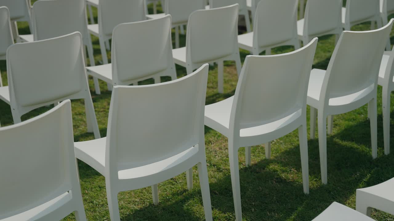 minimalist white chairs set up for outdoor event casting soft shadows on grass