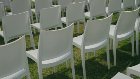 minimalist white chairs set up for outdoor event casting soft shadows on grass
