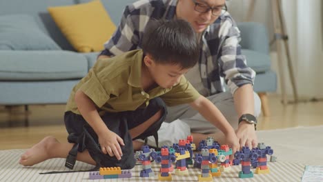 asian father and son assemble the construction set colorful plastic toy brick on a mat at home