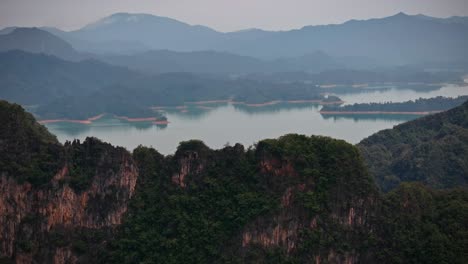 drone footage flying over limestone cliffs in khao sok national park, thailand, revealing rainforest, lake islands, and misty mountains in the distance