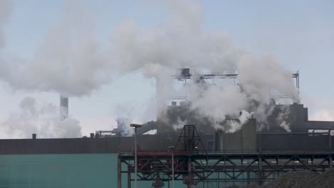 industrial complex emitting large amounts of steam or smoke, cloudy skies above, environmental impact concept