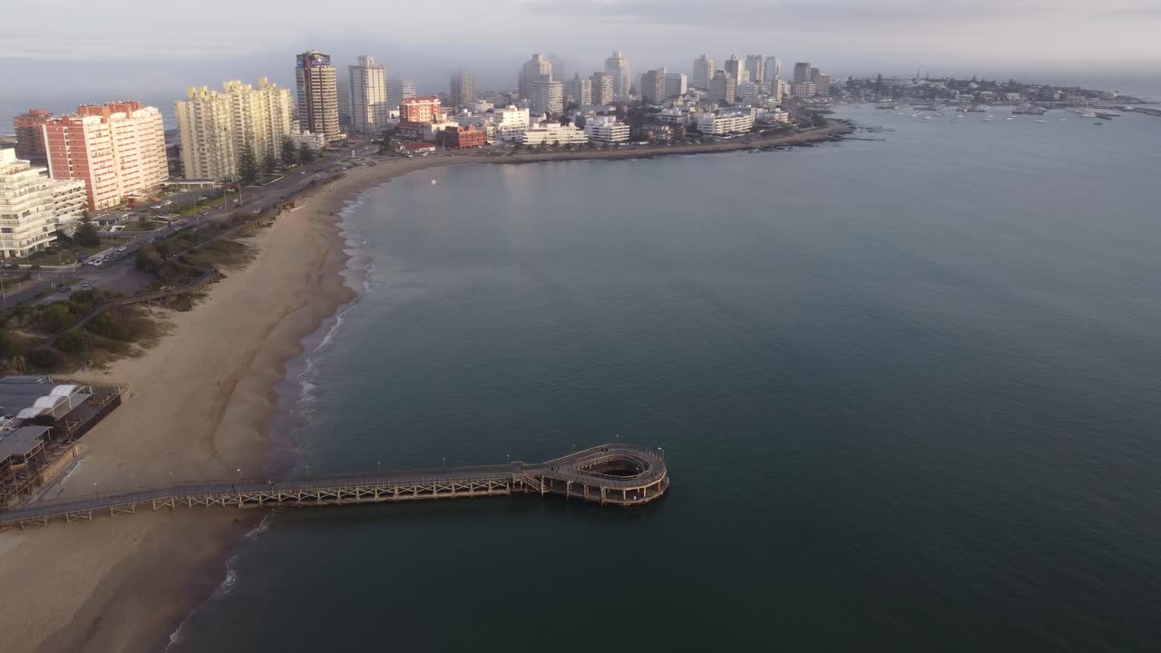 vista aérea que muestra el embarcadero circular y la playa de arena con el horizonte de punta del este en segundo plano durante el día nublado