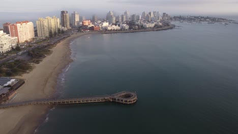 vista aérea que muestra el embarcadero circular y la playa de arena con el horizonte de punta del este en segundo plano durante el día nublado