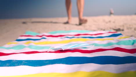 man walks towards beach towel and lays down protective face mask