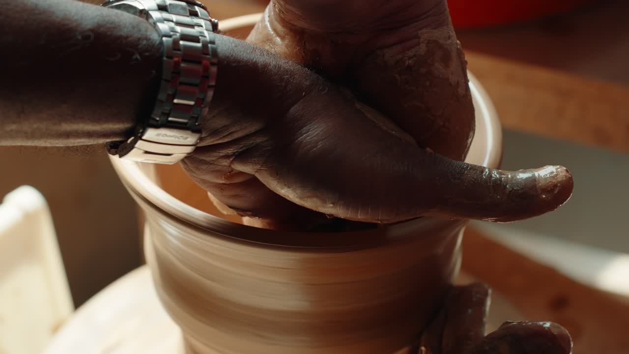 Two men’s hands work together shaping wet clay on a pottery wheel, highlighting a hands-on pottery lesson in warm natural light - close-up