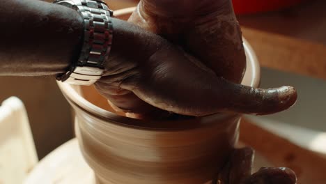 two men’s hands work together shaping wet clay on a pottery wheel, highlighting a hands-on pottery lesson in warm natural light - close-up