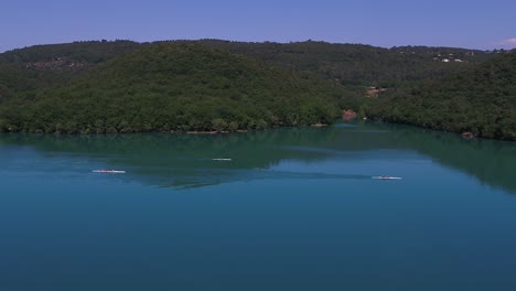 Descending-aerial-view-towards-group-of-rowing-athletes-cruising-woodland-lake-waters