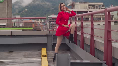 In-Port-of-Spain,-Trinidad,-a-young-girl-with-Hispanic-heritage-stands-on-a-rooftop-in-a-red-dress,-framed-by-tall-buildings