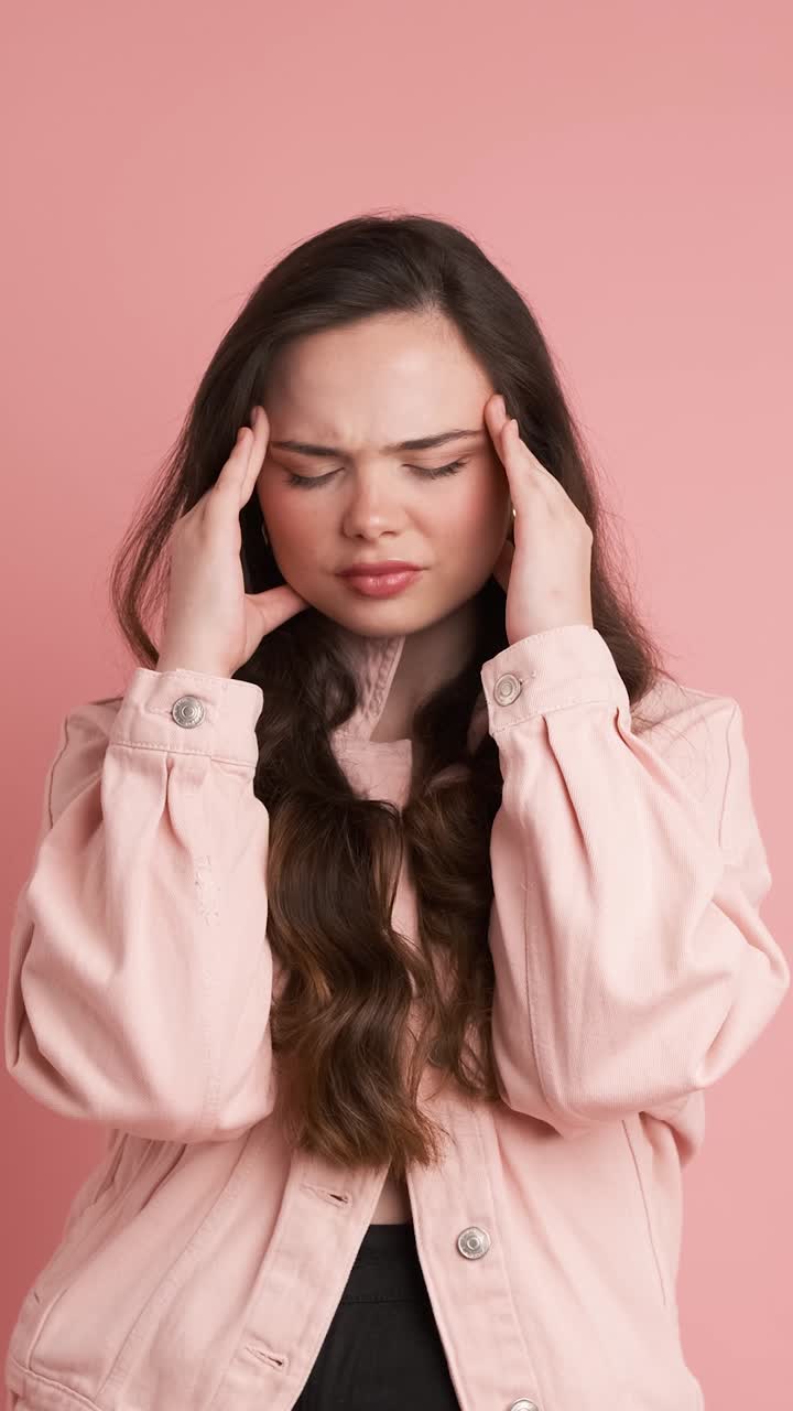 Upset woman suffering from headache in pink studio