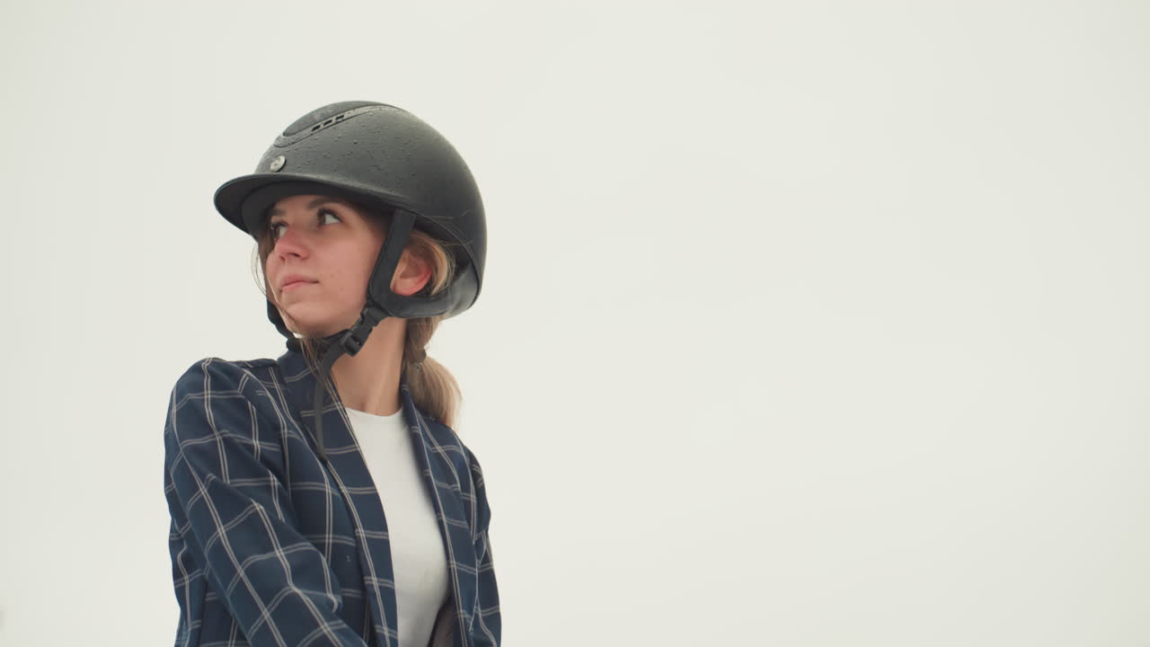 Donna cavaliere con profilo di cavallo in posa, donna con casco che guarda in lontananza, blazer elegante, dolce connessione con il cavallo nero, scena equestre nuvolosa, umore riflessivo durante la lezione all'aperto.