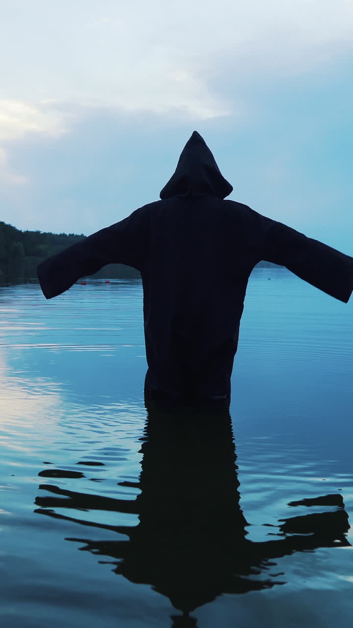 Ghost woman in the water outdoor. Scary figure in black mantle.. Vertical video