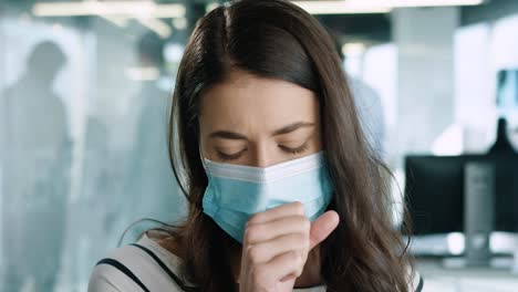 close-up view of caucasian young female patient wearing medical mask and coughing badly while talking indoor in hospital