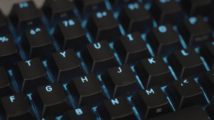 RGB lights in blue shade shining through black keycaps on a modern mechanical keyboard