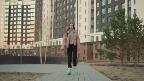 una mujer joven con una chaqueta de melocotón y pantalones negros patinando felizmente a través de un área urbana moderna, con las manos extendidas. el fondo presenta altos edificios residenciales, árboles