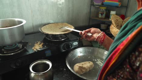 side angle shot of senior aged woman making traditional bhakri and preparing dough in the kitchen of rural india using cooking gas stove