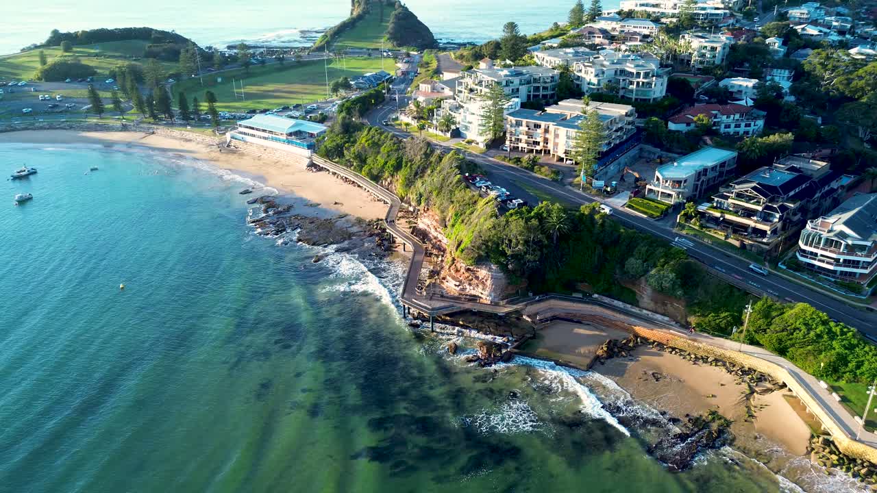 Drone aerial landscape of ocean waves breaking at Terrigal sandy beach bay with boardwalk and town residential housing rural suburb streets Central Coast tourism Australia holidays travel The Skillion