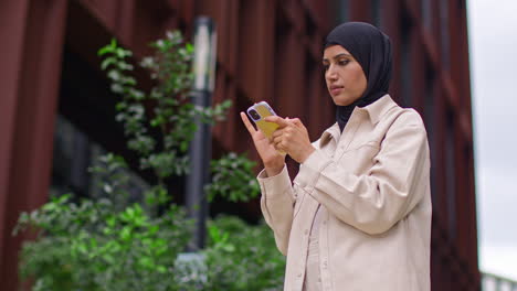 muslim businesswoman wearing hijab going to work standing outside modern office looking at mobile phone 6