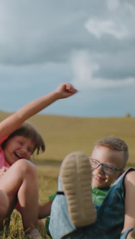 hermanos agachados al aire libre a la luz del sol brillante mientras la hermana sostiene al hermano cerca, ambos sonriendo alegremente mientras la madre captura su momento lúdico con una fotografía, rodeados de campo abierto y exuberante