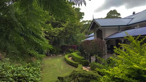 Smooth-cinematic-descending-reveal-shot-of-a-classic-traditional-country-Queenslander-house,-nestling-in-neatly-manicured-landscaped-garden