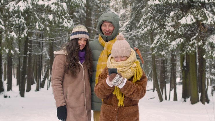 Jeune fille prenant des photos avec un smartphone, vêtue de vêtements d'hiver, dans une forêt enneigée 1.