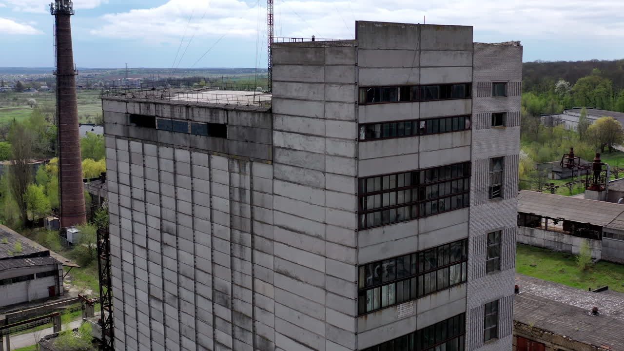 Tall old factory building on green nature background. Abandoned industry. Empty ruined industrial edifices in the countryside. Aerial view.