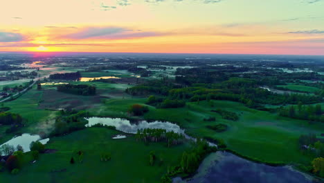 Hermosa-Vista-Panorámica-Rural-De-Los-Campos-Verdes-Y-El-Río-Durante-La-Puesta-De-Sol---Tiro-Amplio-Aéreo